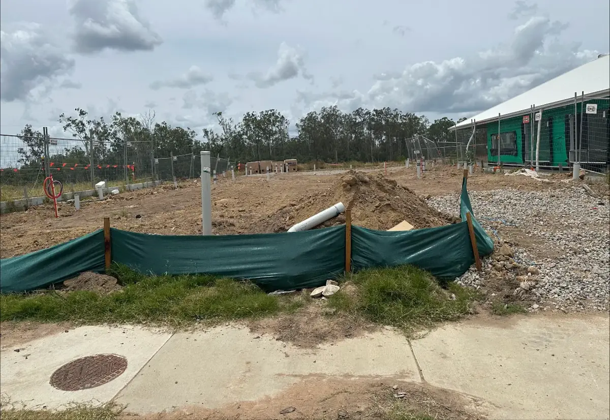 A cleared lot with silt fence and service pipes, waiting for construction