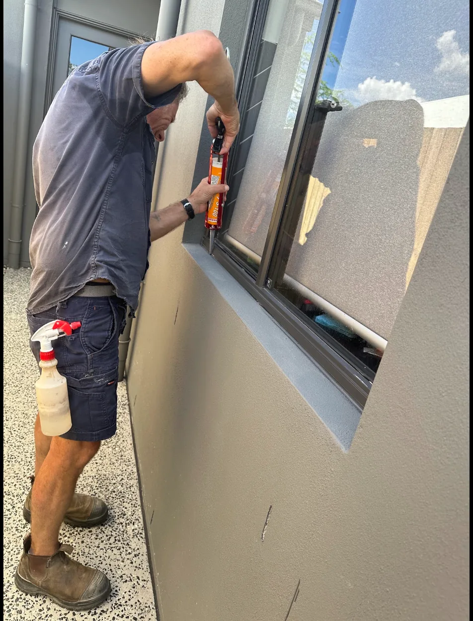 A tradesperson resealing a window frame