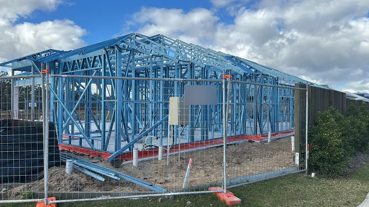 A blue steel house frame behind site fencing